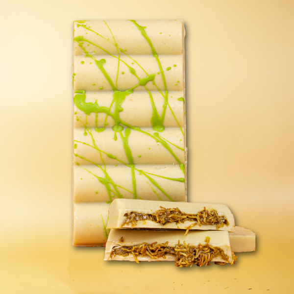 Weiße Schokoladentafel mit grünem Pistazienspritzer, aufgebrochene Stücke davor zeigen die Pistazienfüllung mit Kadayif.