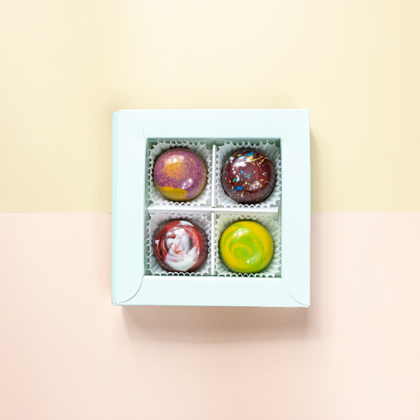 Fruit Lover 4er Pralinenbox von oben — vier fruchtige Pralinen in bunten Tönen, jede einzeln von Hand bemalt.
